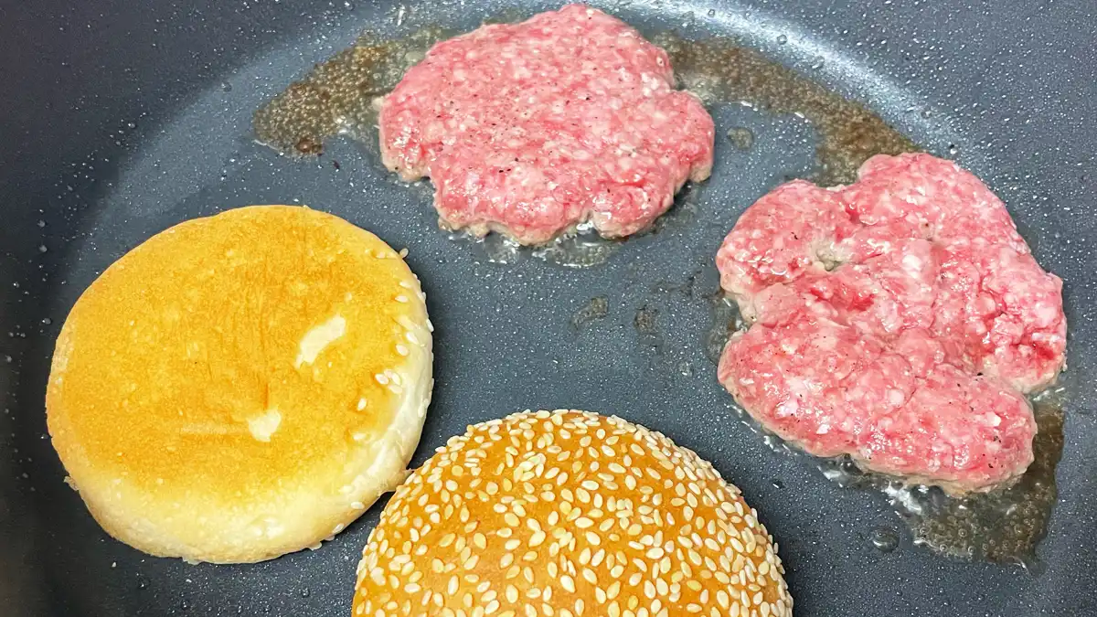 フライパンで潰したパティとバンズを焼いている様子