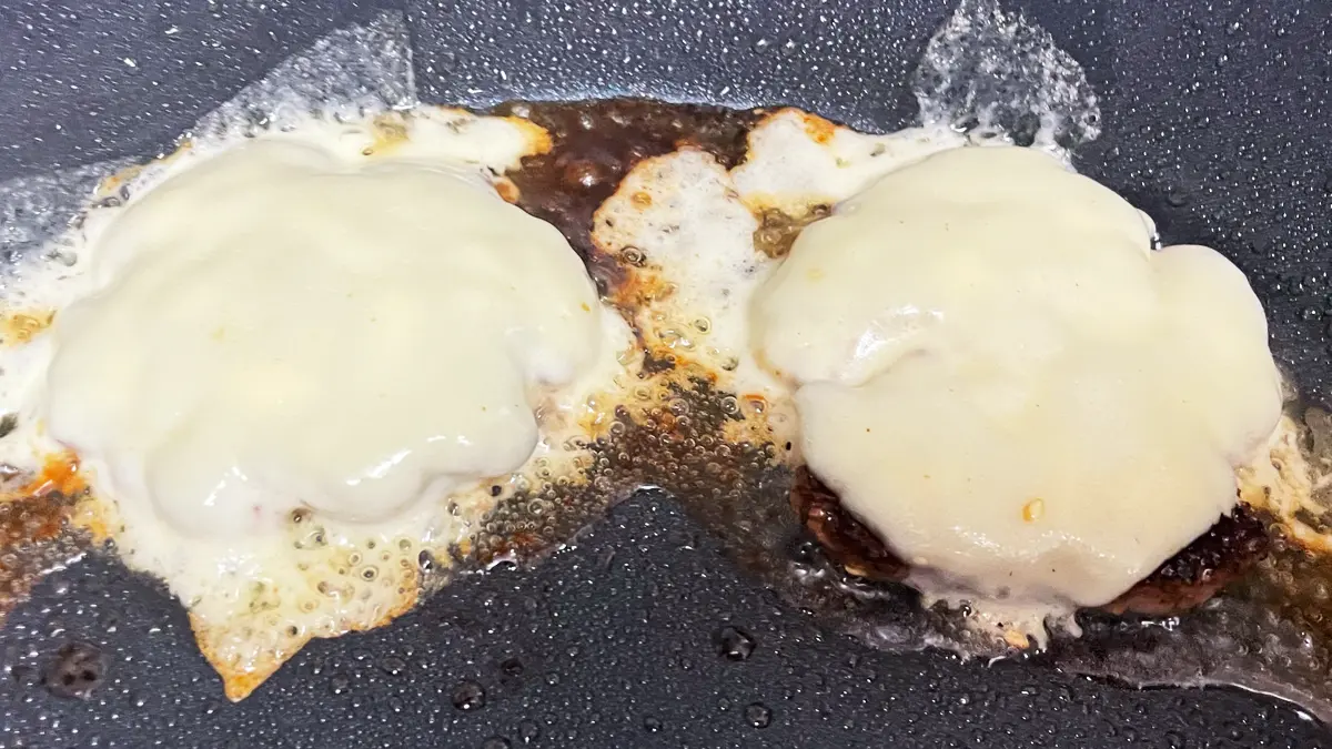 フライパンで焼いているパティの上にとろけるチーズを乗せた様子