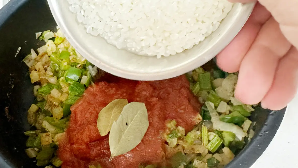 炒めた野菜(Holy Trinity)にカットトマトとローリエ、そして研いだ米を入れる様子