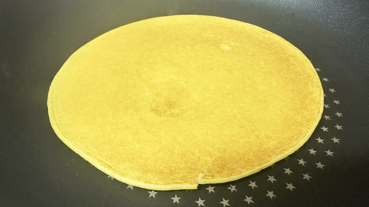 薄焼き米粉パンケーキをフライパンで焼いている様子。焦げ目がうっすらついている