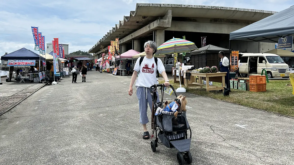 大原漁港の土曜マーケット参加ブースの並びをバックに、カートに乗ったテリリアンとけい(親びん)